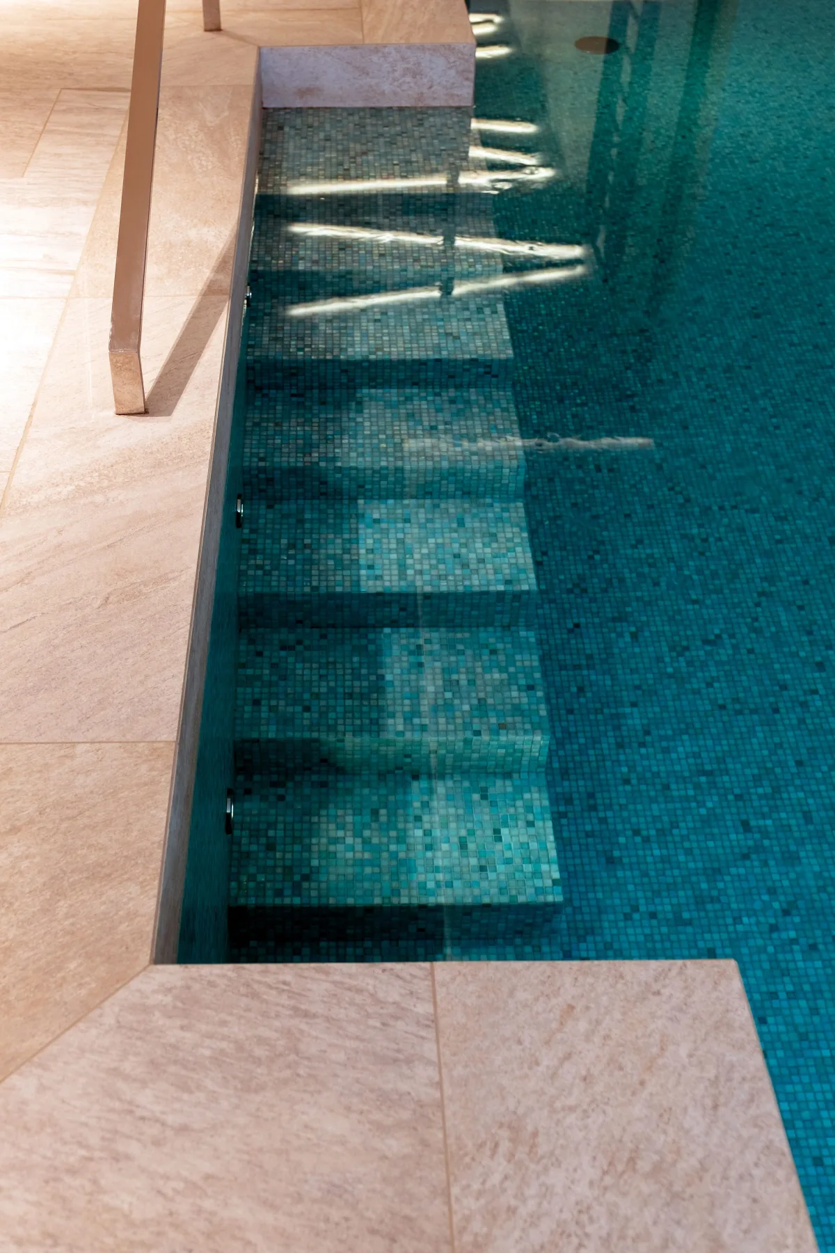 Mosaikbelegte Treppe eines Innenpools, Naturstein und türkis schimmerndes Wasser