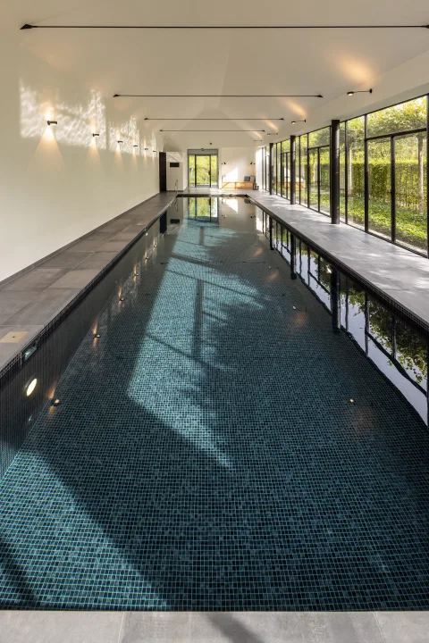 Lange Schwimmhalle mit dunklem Mosaik und raumhoher Fensterfront