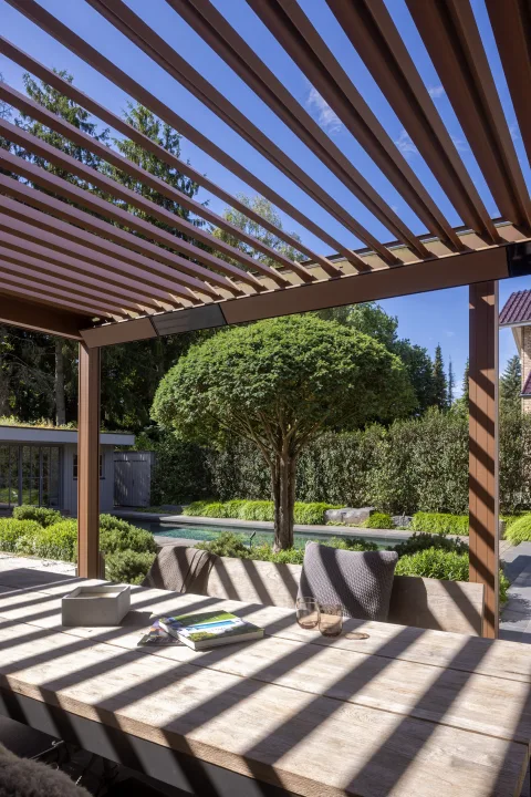 Blick unter einer Lamellenpergola über den Esstisch in den Garten mit Becken