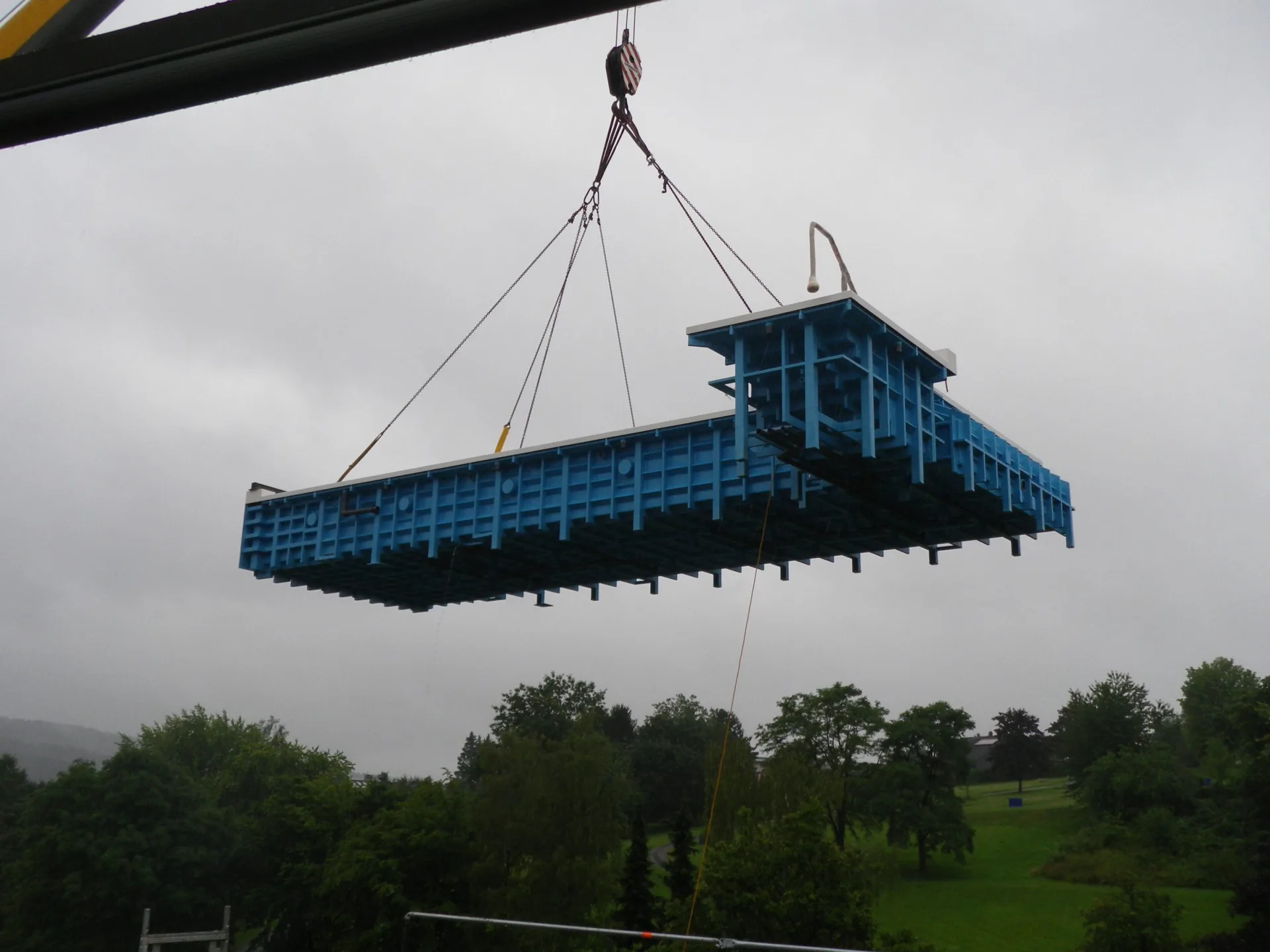 Ein Beckenkörper wird von einem Kran über eine Baustelle gehoben