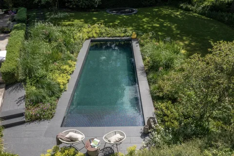 Beleuchtetes Becken in der Dämmerung, dahinter Garten und Waldrand