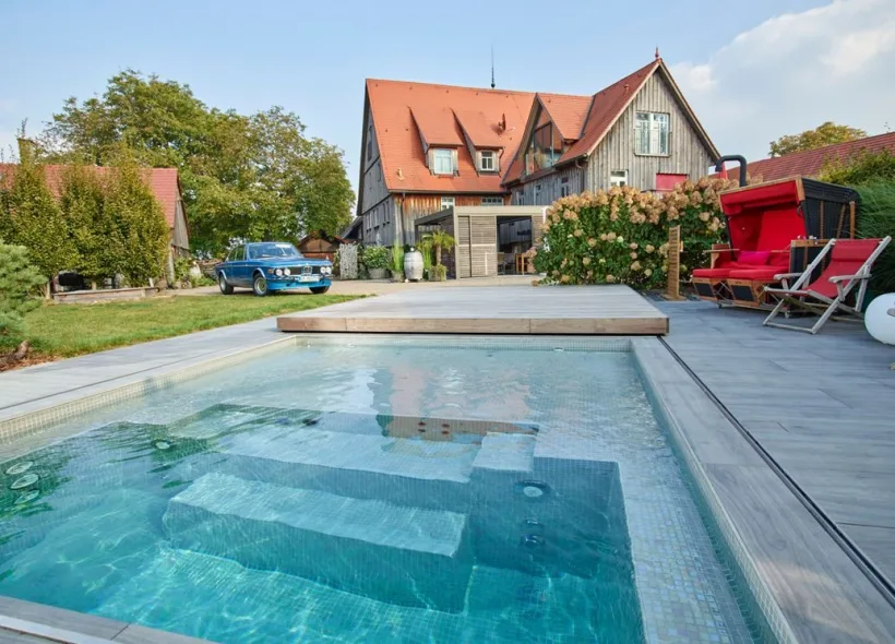 Becken mit Sitzstufen vor einem Landhaus, Strandkorb und Liegestühle auf der Terrasse