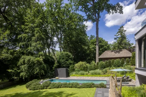 Becken in einer Gartenlandschaft mit Trockenmauer und altem Baumbestand, Sonnenschirm und Liegen