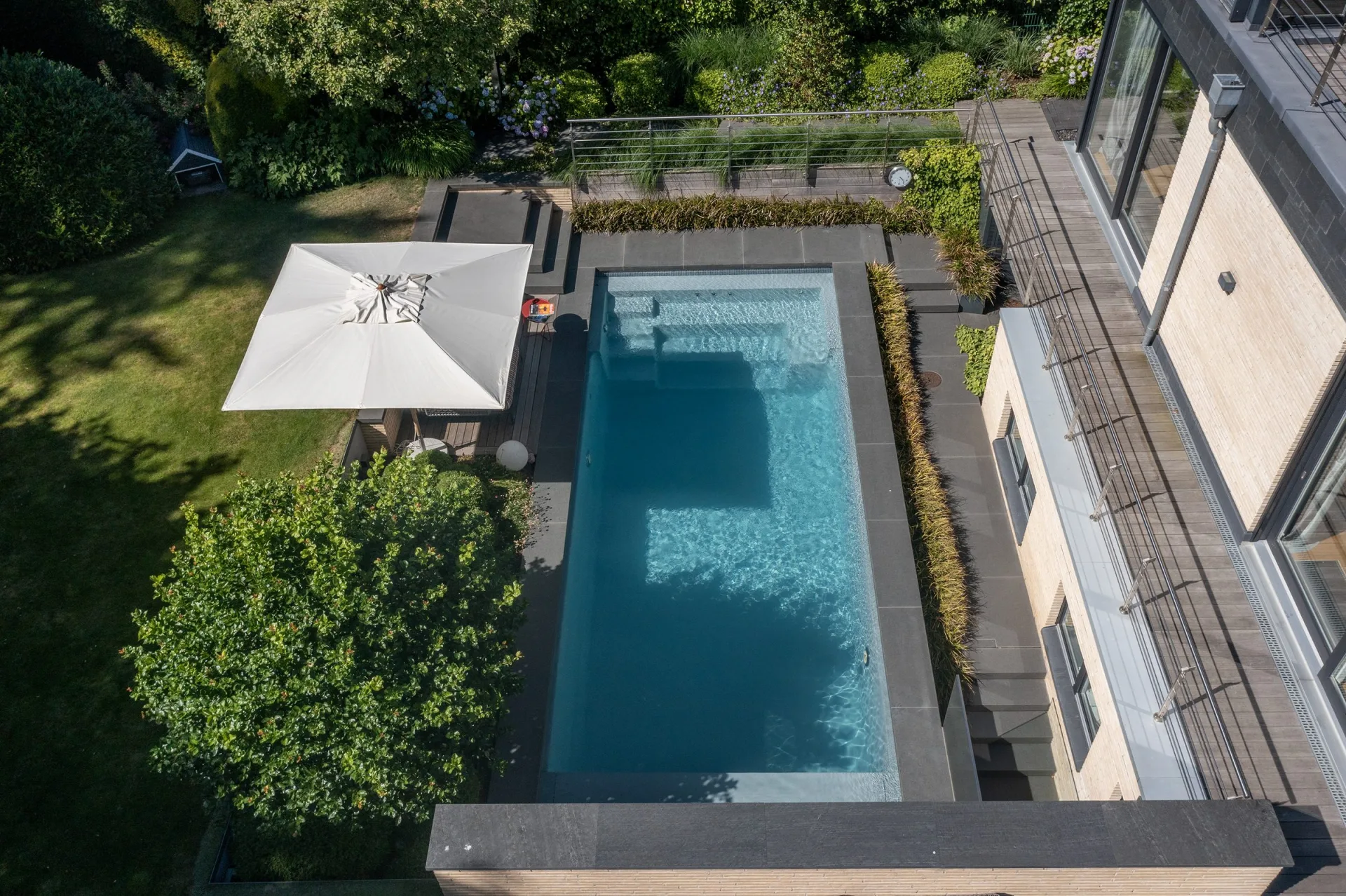 Luftbild einer Gartenanlage mit rechteckigem Pool, Terrasse und Sonnenschirm