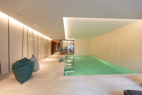 Helles Hallenbad mit grün schimmerndem Wasser, Lichtvoute und verglastem Fitnessbereich