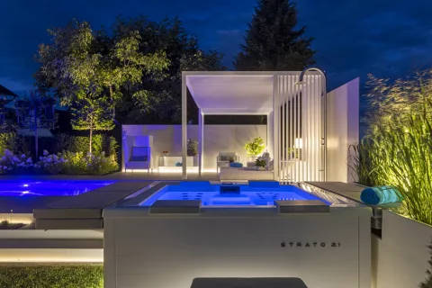 Beleuchteter Whirlpool bei Nacht, dahinter Pavillon und blau leuchtendes Becken