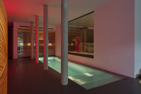 Innenbecken zwischen Betonstützen, dahinter Sauna und Lounge hinter raumhohem Glas